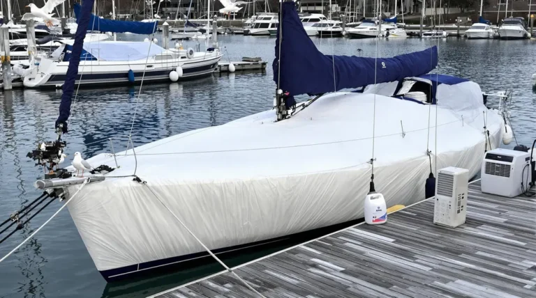 Bateaux recouverts de bâches dans une marina en hiver, avec de la neige tombant doucement.